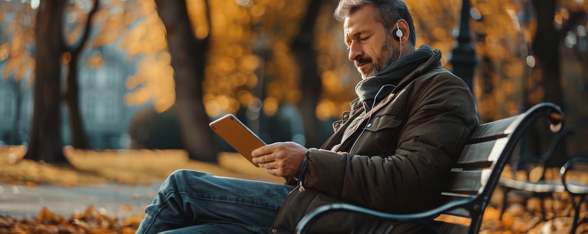 Mann lernt kostenlos Italienisch mit Smartphone und Kopfhörern auf einer Parkbank