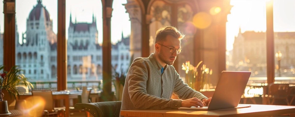 Person lernt Ungarisch am Laptop in einem Café mit Budapest im Hintergrund