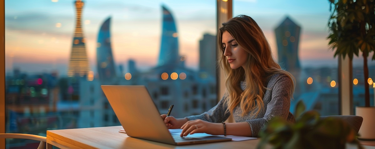 Junge Frau lernt Aserbaidschanisch am Laptop mit einem Notizbuch, im Hintergrund die Skyline von Baku