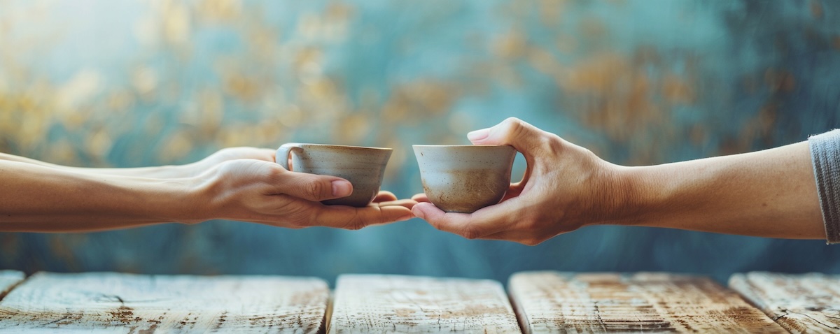 Zwei Hände reichen einander eine warme Teetasse, Symbol für Danke auf Ukrainisch (Дякую)